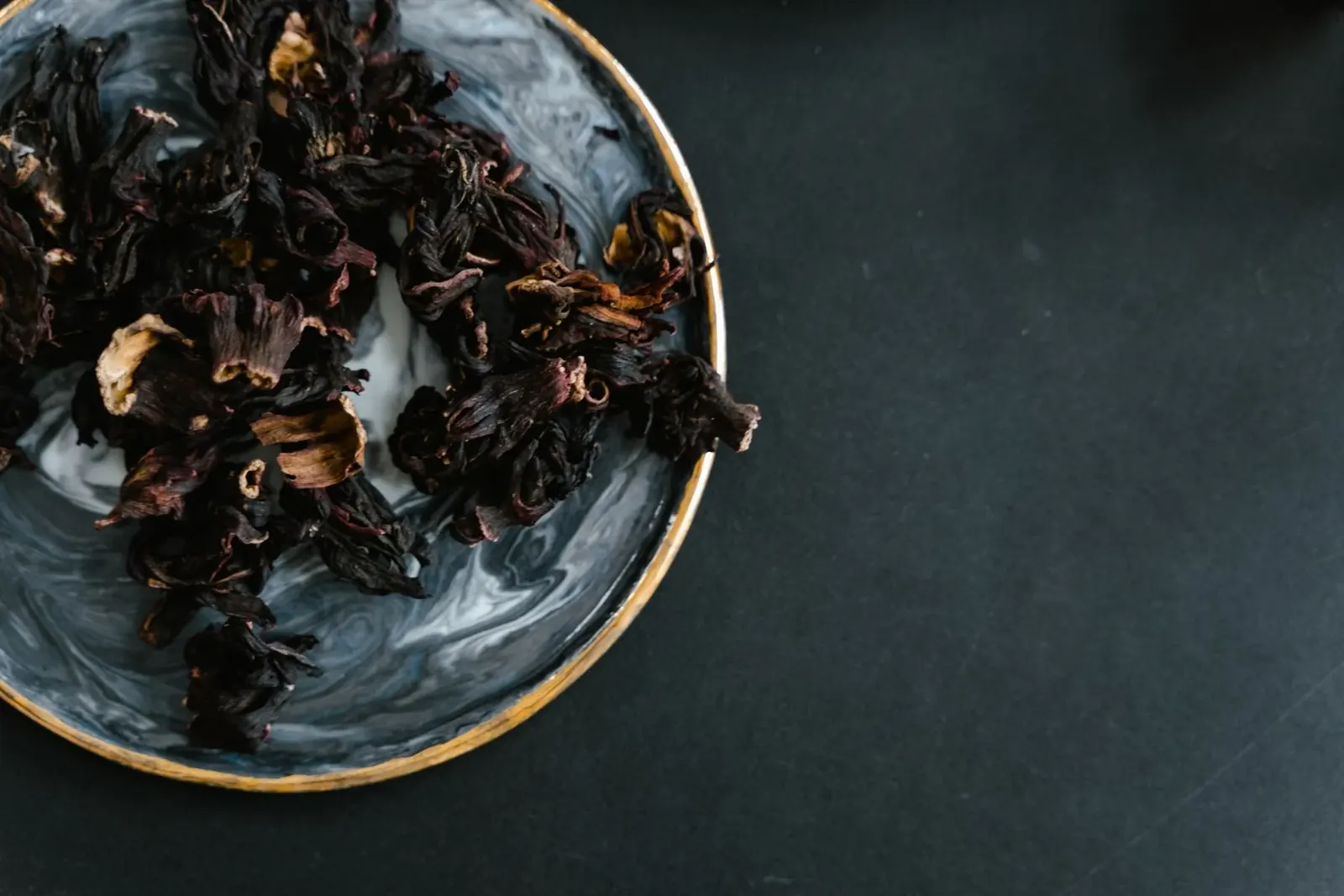 Deep red dried hibiscus flowers in a marble bowl